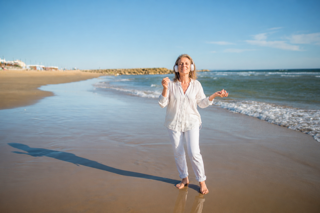 Woman dancing on the beach with headphones on.