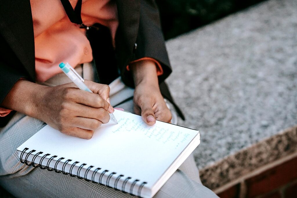 person writing goals and ideas in spiral notebook